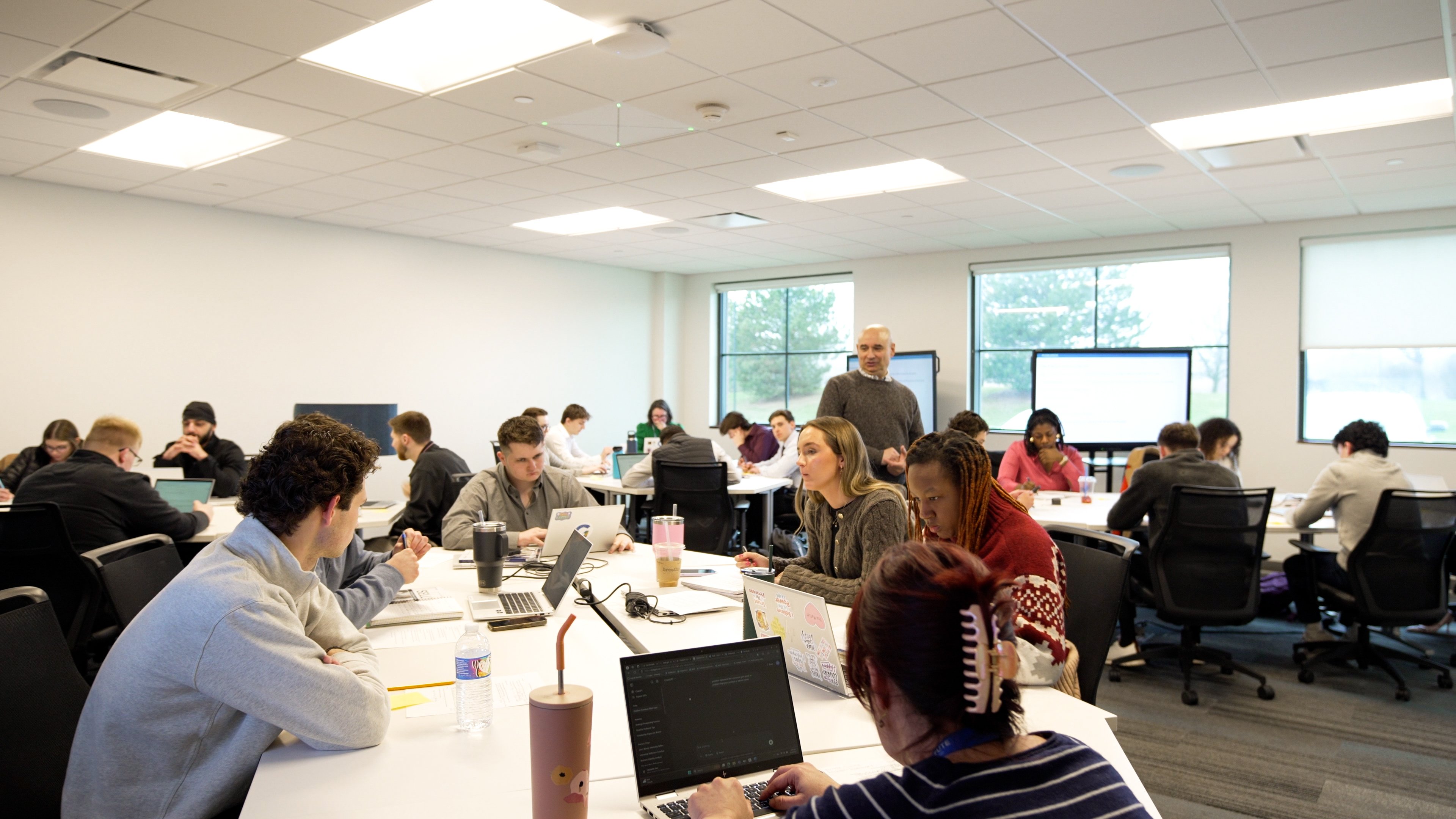 Students collaborating using laptops and AV technology at the Golisano Institute classroom.